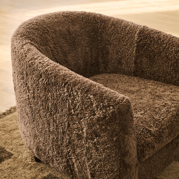 Rounded accent chair upholstered in a brown shearling fabric