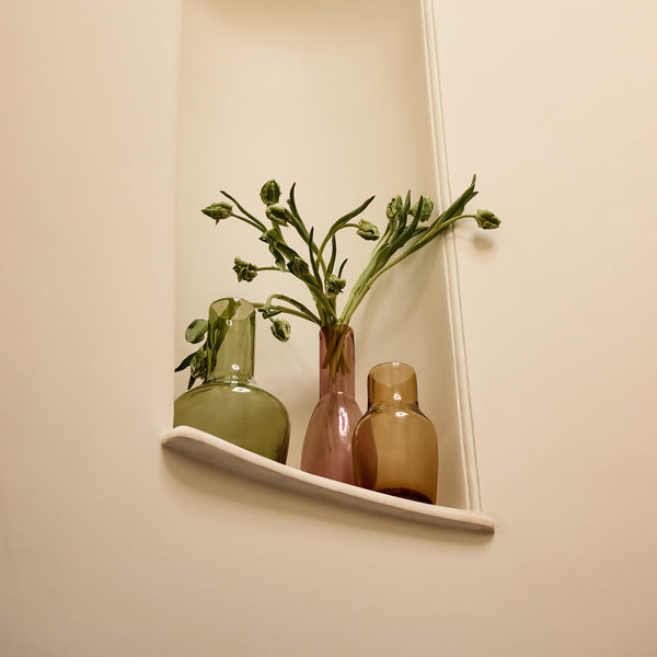 A collection of 3 parlor glass vases in green, amethyst and amber. Green stems jut out of the amethyst vase.