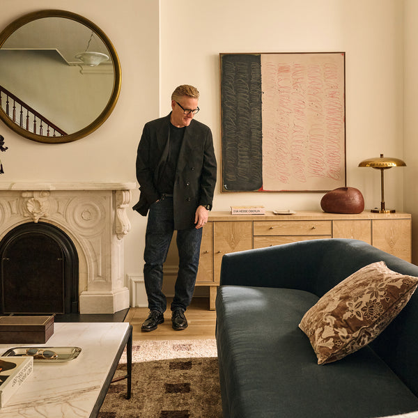 Todd stands beside the fireplace with his jacket swapped for a black suit jacket over his black t-shirt and dark jeans. He is wearing black dress shoes.